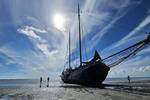Die Tjalk Aagtje liegt bei Ebbe im Watt, mit Menschen neben dem Schiff