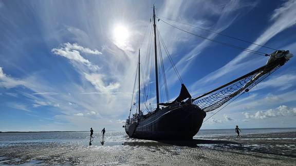 Die Tjalk Aagtje liegt bei Ebbe im Watt, mit Menschen neben dem Schiff