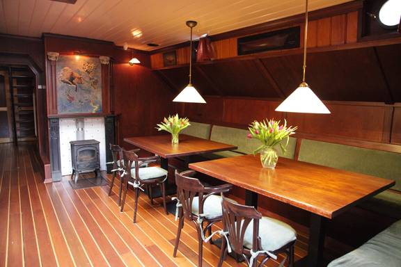 Salon der Aldebaran mit Holzesstischen und roten Sitzbänken
