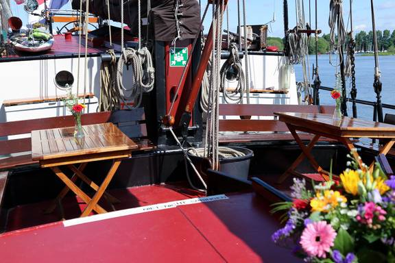 Sitzbereich mit Holztischen und Blumen an Deck der Avondrood