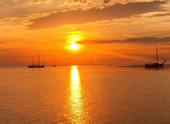 Oranger Sonnenuntergang über dem Wasser mit Segelschiffen am Horizont