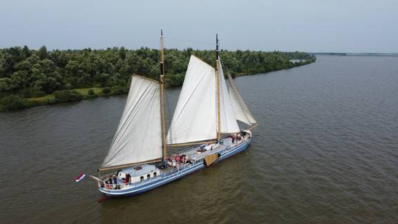 Luftaufnahme der De Hester unter Segeln an einem grünen Ufer