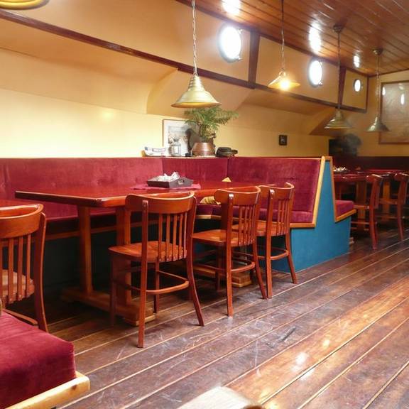 Salon der Gouwzee mit Holzesstischen und roten Sitzbänken