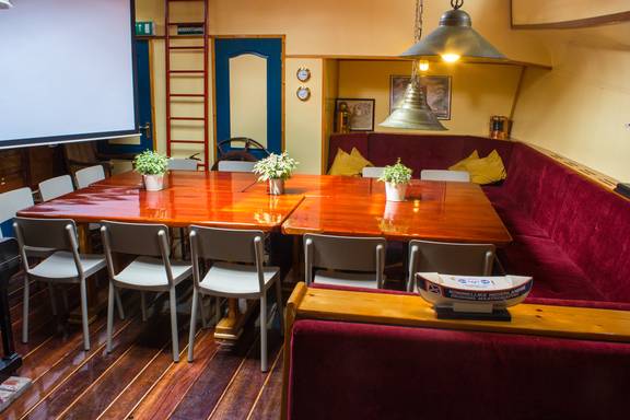 Salon der Gouwzee mit Holzesstischen und roten Sitzbänken