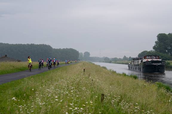 Radgruppe auf dem Deich an einem Kanal, mit dem Passagierschiff Magnifique III