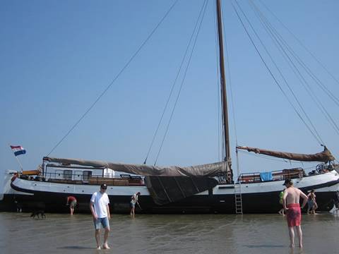 Tjalk Nieuwe Zorg im Watt trockengefallen mit Gästen neben dem Schiff