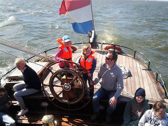 Gäste am Steuerrad auf dem Achterdeck der Pelikaan
