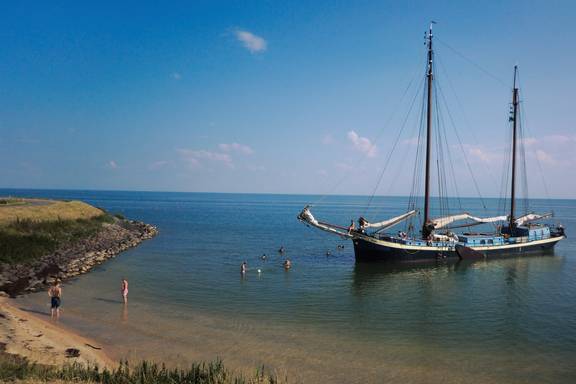Sybaris liegt neben einem sandigen Ufer vor Anker