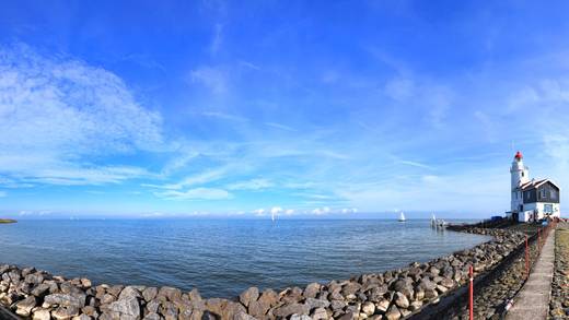 Blauer Himmel über dem IJsselmeer mit steinigem Ufer und Leuchtturm
