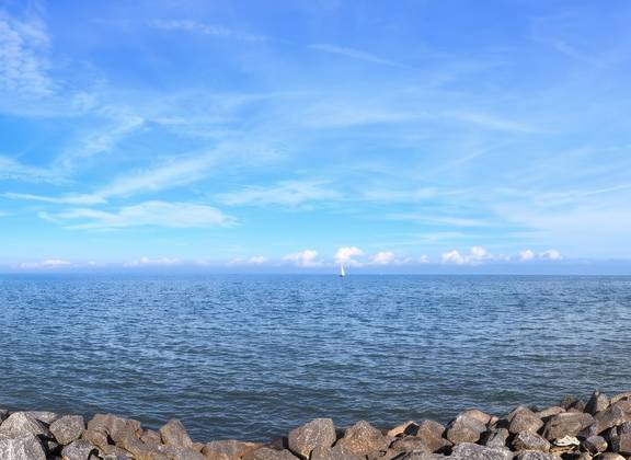 Blick über das IJsselmeer entlang eines steinigen Ufers und eines Leuchtturms