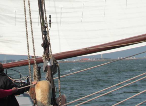 Gäste an Deck unter einem gesetzten Segel mit Blick über das Wasser